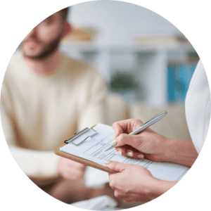 Im Vordergrund eine Frau mit Klemmbrett, die Notizen macht, während im Hintergrund ein Patient entspannt auf einer Couch sitzt – Darstellung einer professionellen therapeutischen Sitzung.